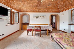 A room with a brick ceiling, a bed, a table with chairs, a TV, and a beach-themed wall art.