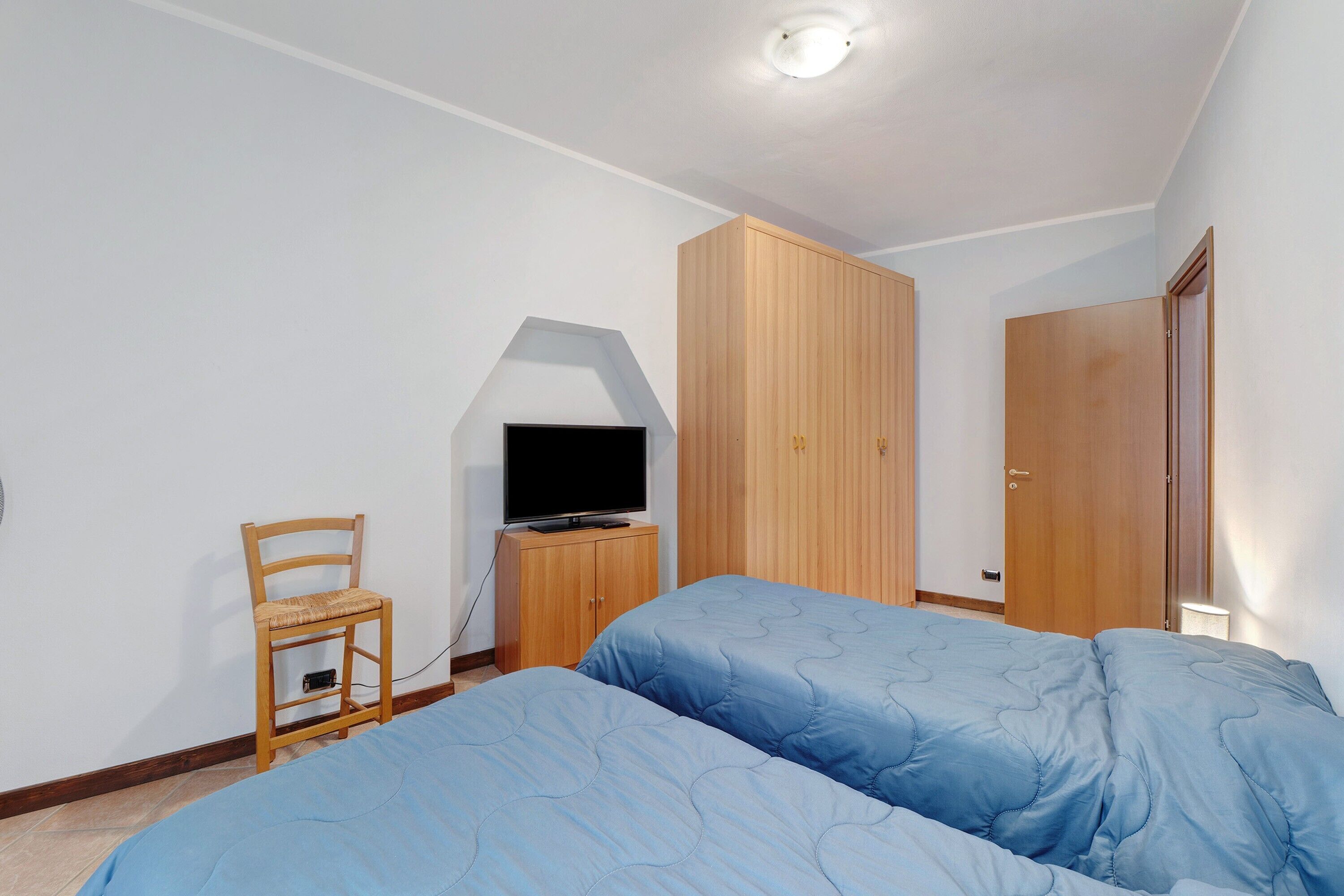 Ein Schlafzimmer mit zwei Betten, einem Holzschrank, einem Fernseher auf einem Schrank und einem Sessel.