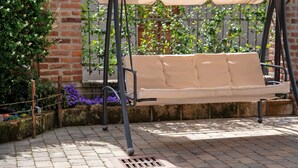 A garden patio with a swing chair, brick walls, and a metal fence. - Apartment 'Centenario Affittacamere' with Wi-Fi and Air Conditioning (Fara Novarese)