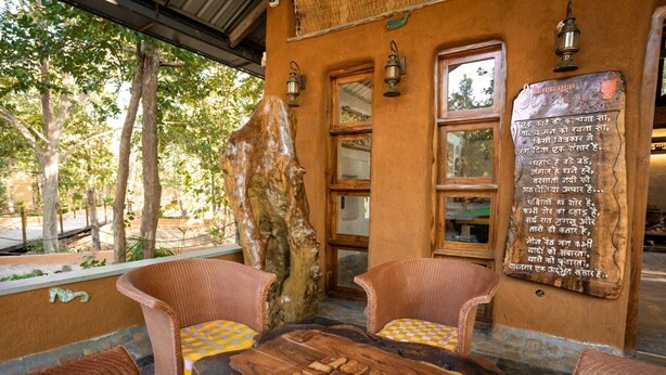Un espace extérieur aménagé dans un style rustique, avec des chaises en osier et une table en bois, un grand tronc d’arbre et une enseigne fixée au mur.