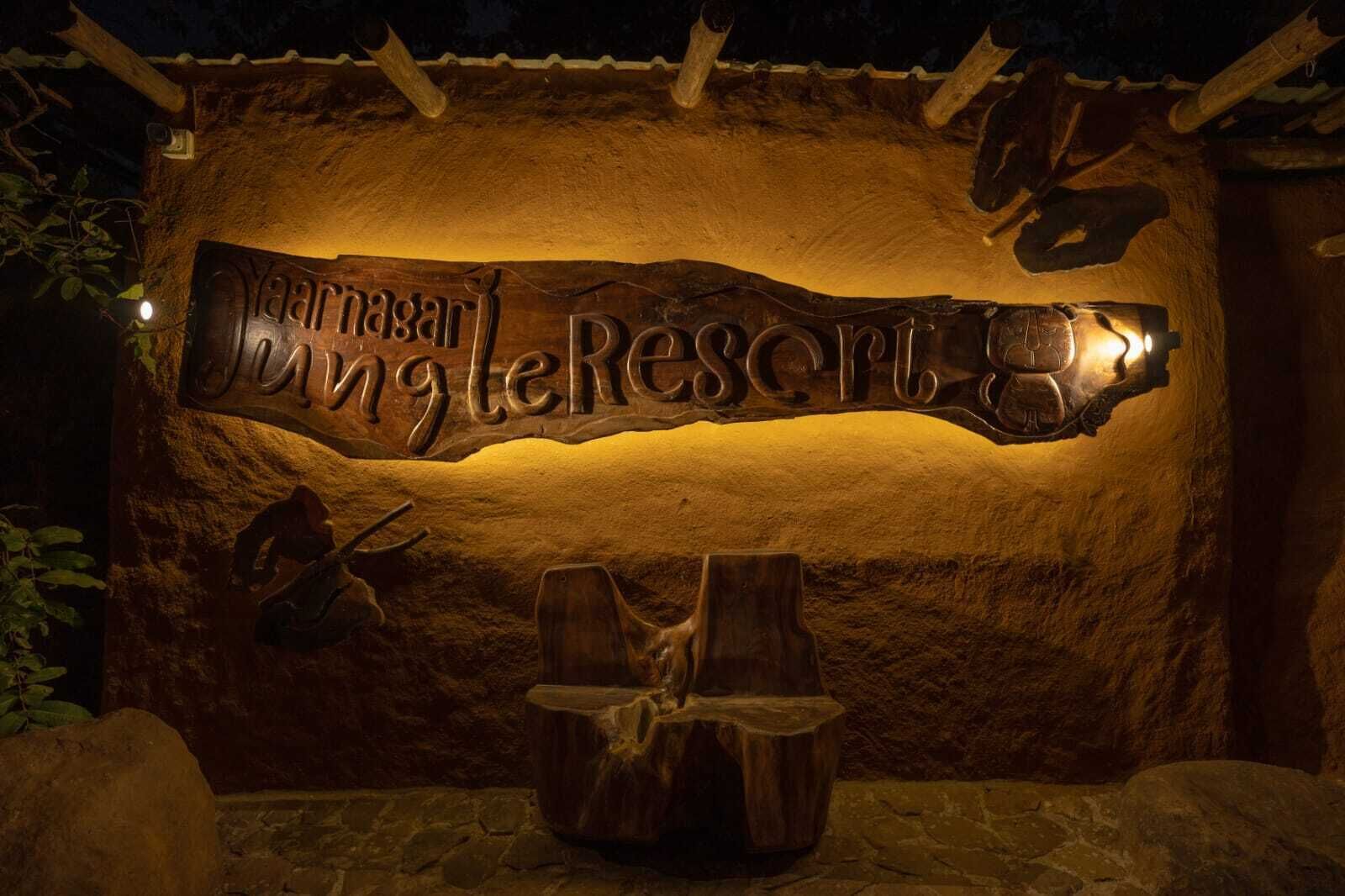 Un letrero de madera con el texto 'Yaar Nagar Jungle Resort' iluminado por una luz.