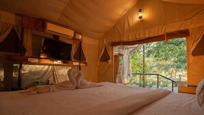 Una habitación con carpa, una cama, un televisor y vistas a árboles.