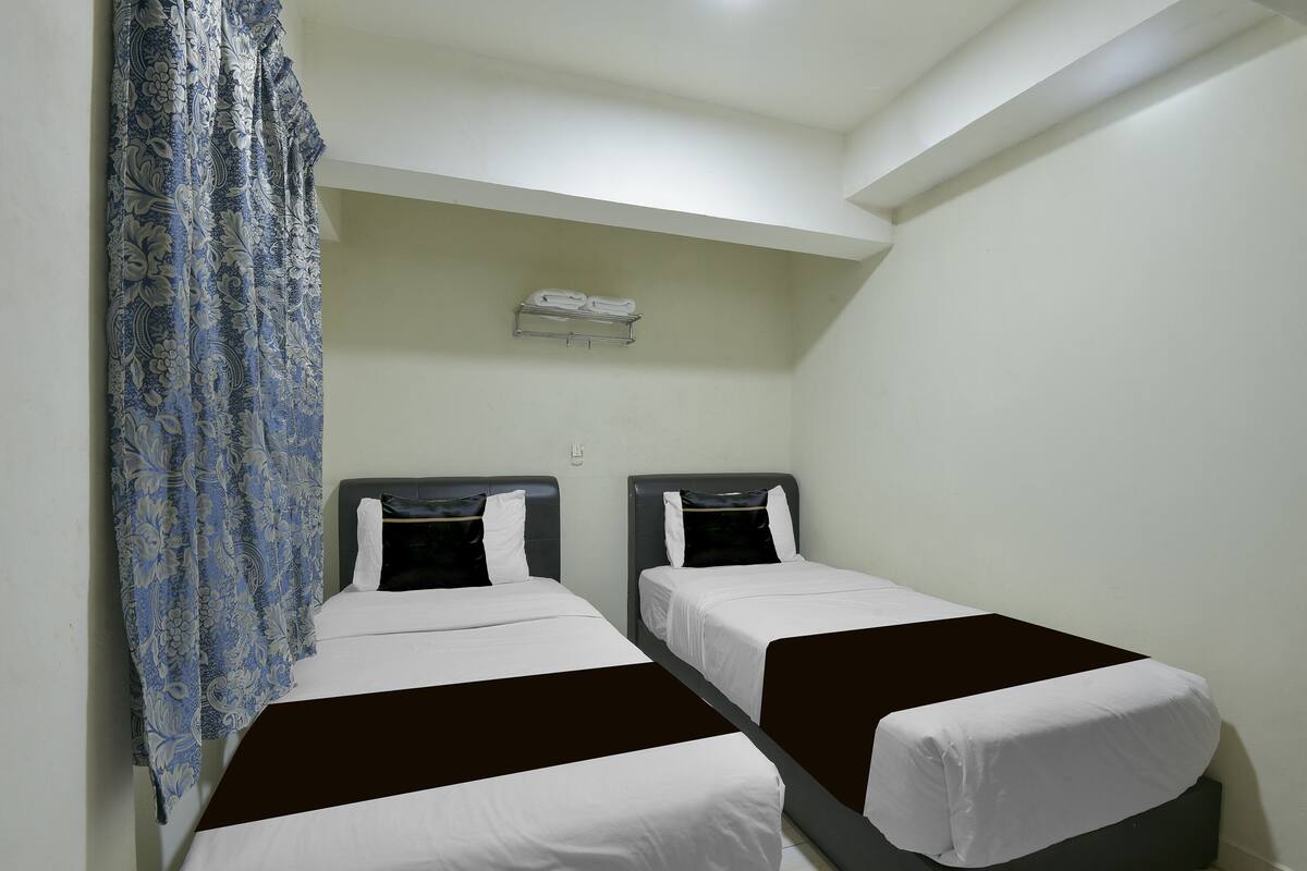 Una habitación con dos camas, una cortina colgante y un estante con toallas.