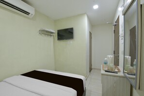 A hotel room with a bed, a TV, a mirror, a small table with toiletries, and an air conditioning unit.
