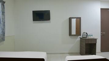 Habitación de hotel con dos camas, televisión, espejo, una mesita con hervidor y vasos, y una puerta.