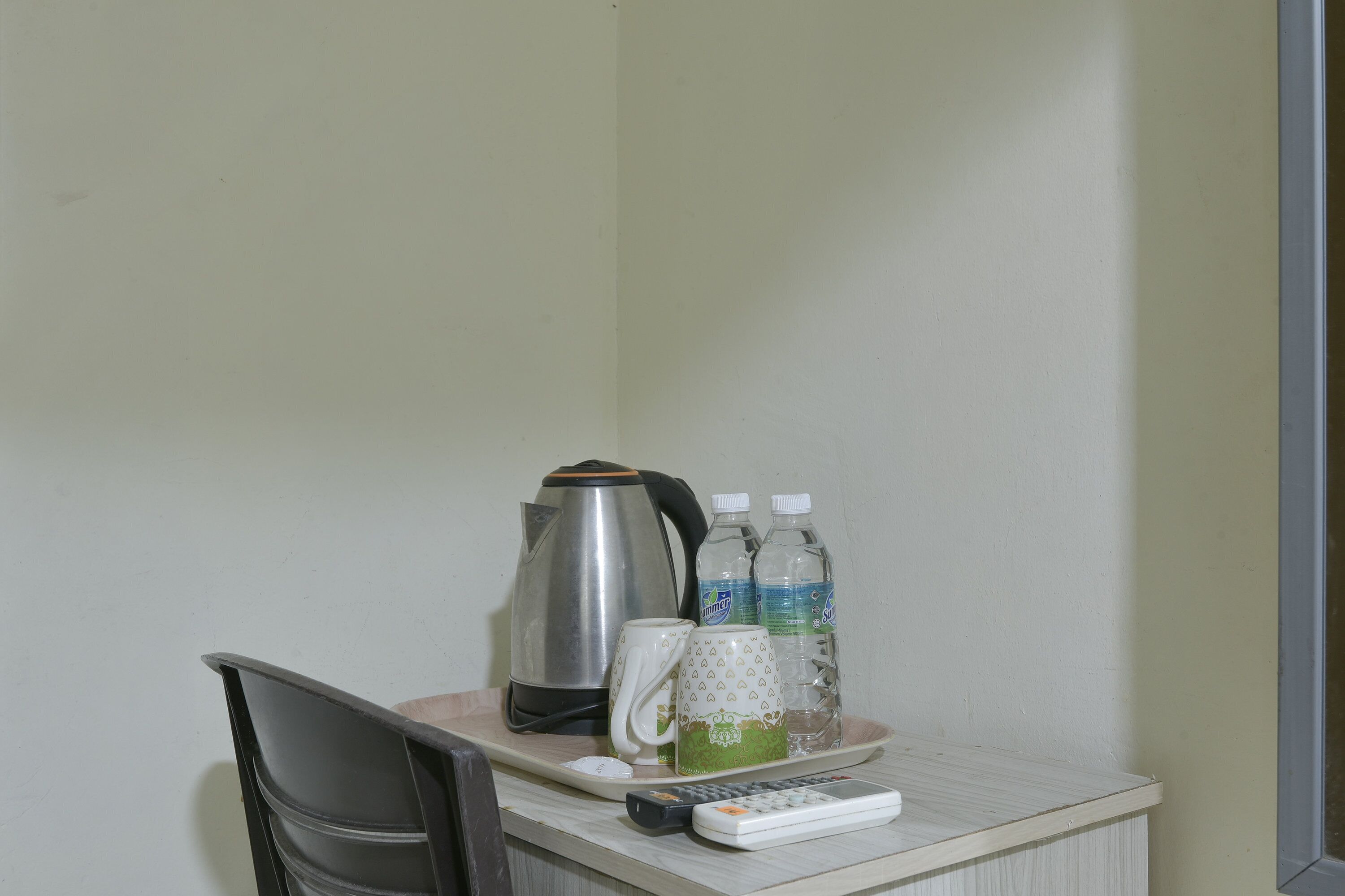 A small table with a kettle, two bottles of water, a mug, and a remote control.