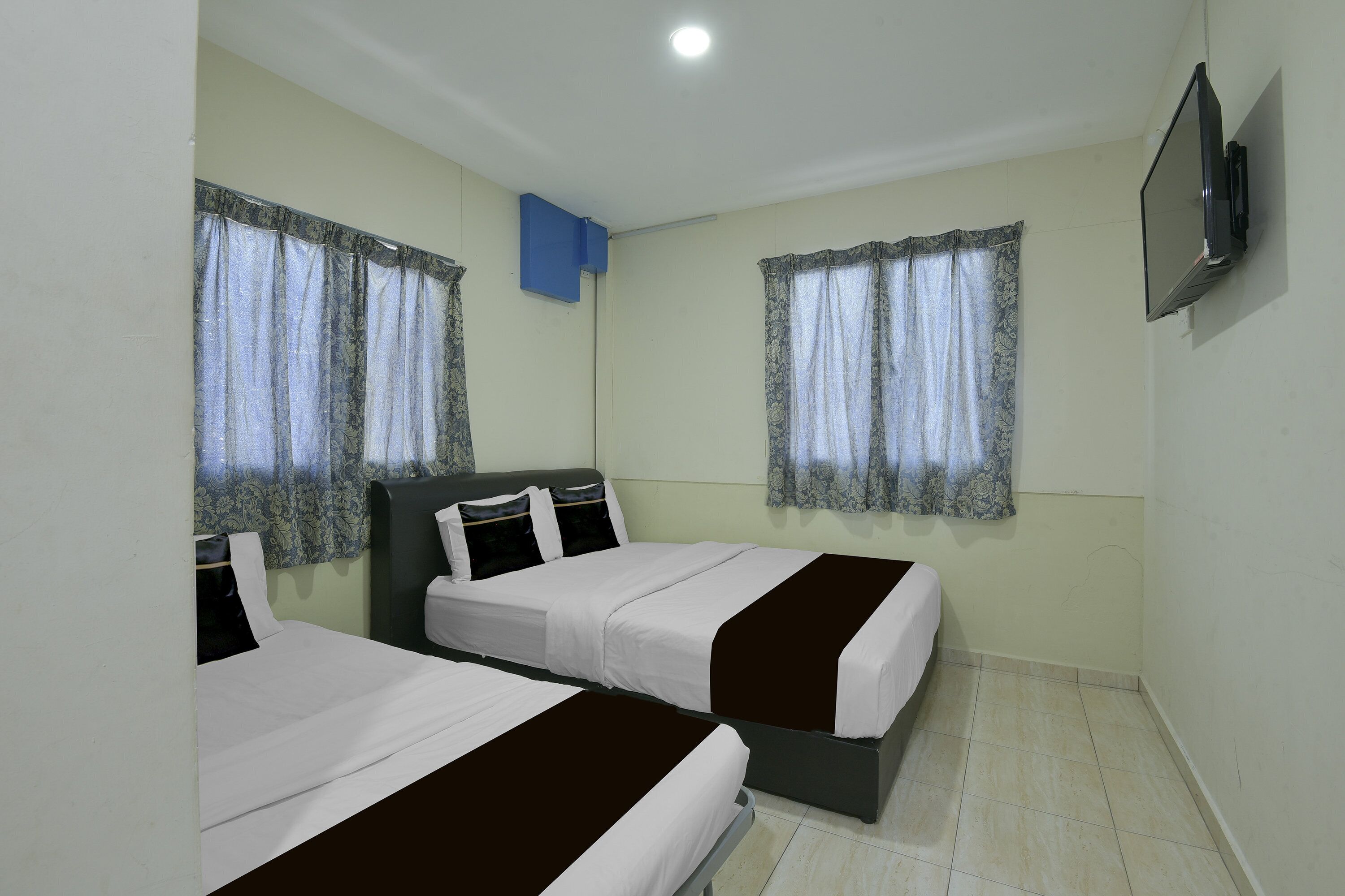 A room with two beds, a flat-screen TV mounted on the wall, and a window with a curtain.