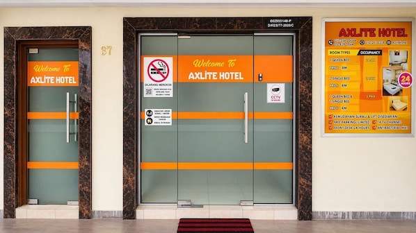Dos puertas del HOTEL AXLITE con un cartel de bienvenida, un letrero de prohibido fumar y un aviso de CCTV.
