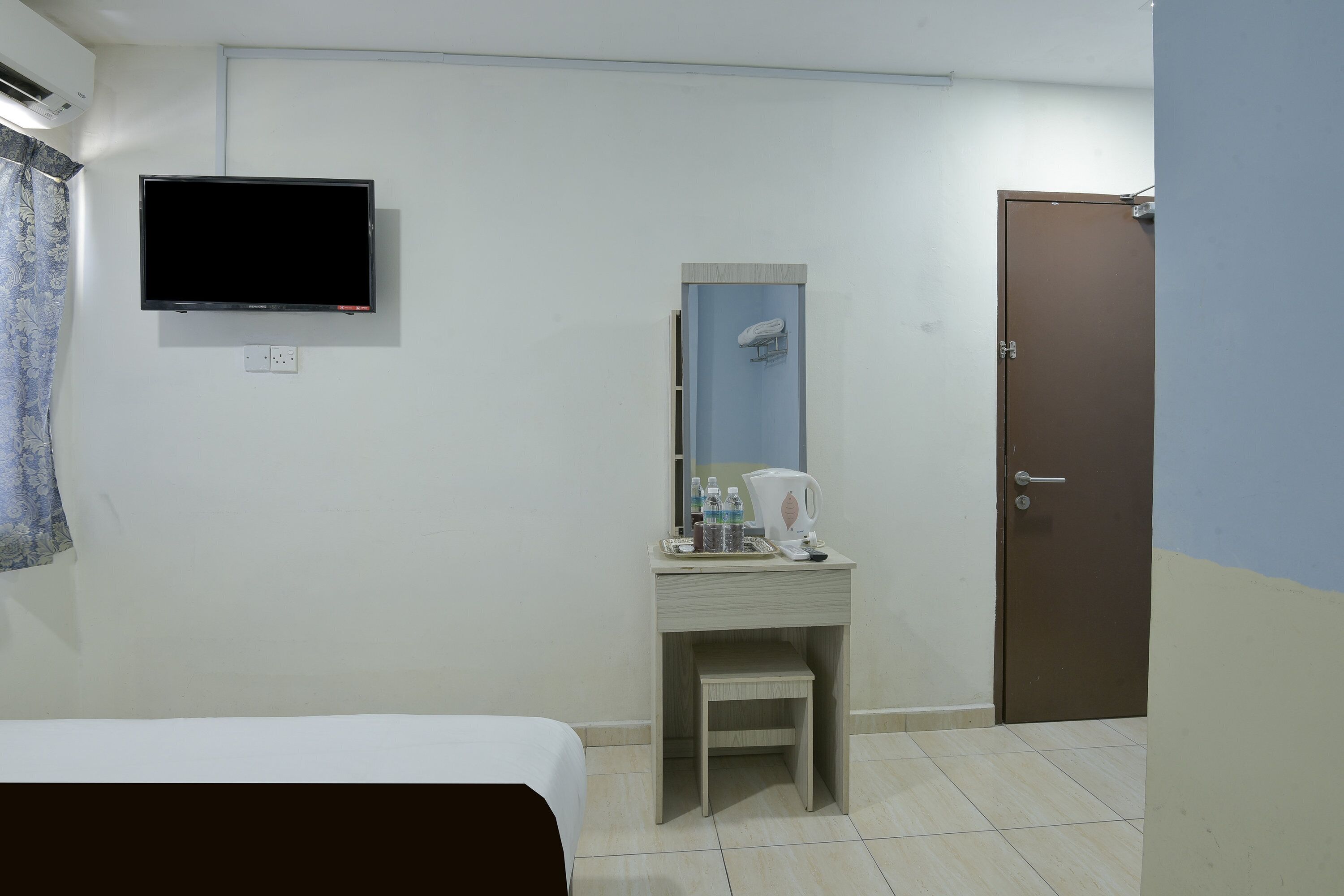 Una habitación de hotel con cama, escritorio con espejo, televisión, puerta y ducha.