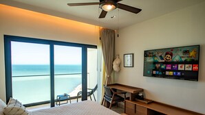Quarto de hotel com cama, escrivaninha, cadeira, televisão e vista para o oceano.