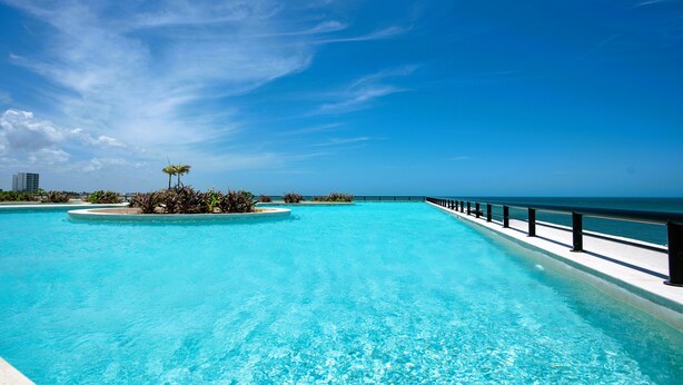 Céu azul límpido, piscina e vista para o oceano.
