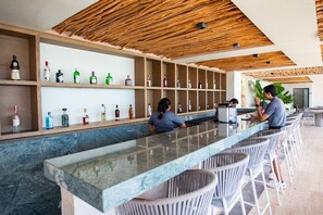 Un espace bar doté d’un long comptoir, de plusieurs étagères remplies de bouteilles et de tabourets de bar en osier.