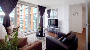 A modern living room with a sofa, a coffee table, a TV, and large windows with curtains.