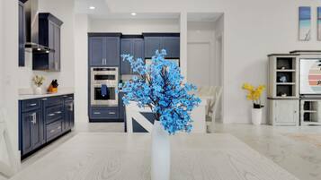 A modern kitchen with dark cabinets, a white vase with blue flowers, and a dining area with a wooden table.