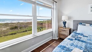 Quarto com uma janela grande, uma cama, uma mesa de cabeceira e vista para a praia.