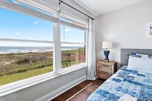 Ein Schlafzimmer mit großem Fenster, einem Bett, einem Nachttisch und Blick auf den Strand.