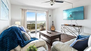 Uma sala de estar com sofá, mesa de centro e televisão exibindo um surfista.