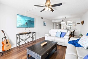 Ein Wohnzimmer mit Fernseher, Gitarre, Couchtisch, Sofa und Deckenventilator.
