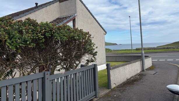 A building with a grey fence, a street lamp, and a view of the sea.