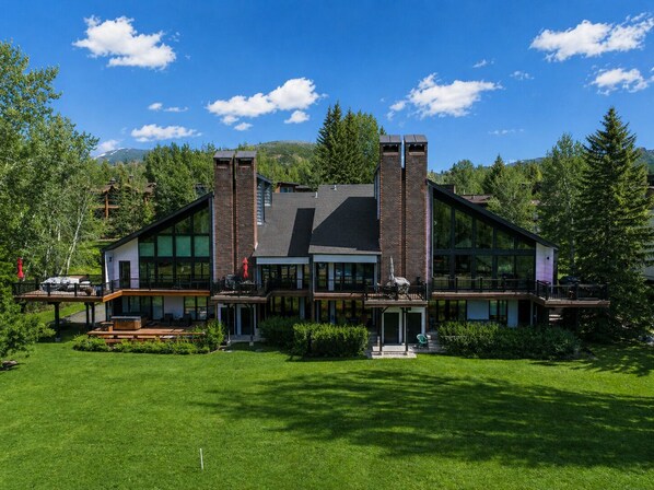 A modern two-story house with large windows, a deck, and a well-maintained lawn.