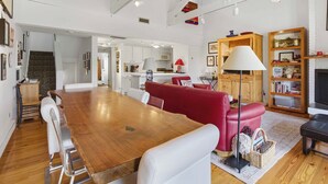 A spacious living area with a wooden dining table, red and white furniture, a fireplace, and a kitchen in the background. - Classic Sun Valley on Hole 1 | Golf Course + Baldy Views (Ketchum)
