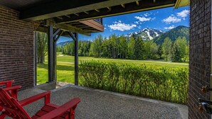 A covered outdoor area with a view of a mountain landscape, a red bench, and a brick wall. - Classic Sun Valley on Hole 1 | Golf Course + Baldy Views (Ketchum)