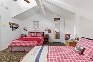 A bedroom with two beds, a sloped ceiling, a mirror, and a door.
