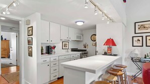 A modern kitchen with white cabinets, a central island with stools, a microwave, and a red lamp. - Classic Sun Valley on Hole 1 | Golf Course + Baldy Views (Ketchum)
