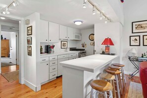 A modern kitchen with white cabinets, a central island with stools, a microwave, and a red lamp. - Classic Sun Valley on Hole 1 | Golf Course + Baldy Views (Ketchum)