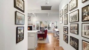A hallway with framed photographs on the walls, a kitchen area with a red chair, and a wooden bench. - Classic Sun Valley on Hole 1 | Golf Course + Baldy Views (Ketchum)