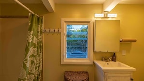 Une salle de bain avec une fenêtre, un lavabo, un miroir, un porte-serviettes et un panier en osier.