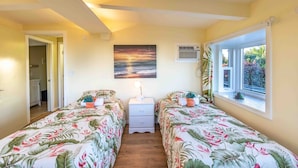 Une chambre avec deux lits, une table de chevet, un tableau, un appareil de climatisation et une fenêtre donnant sur un paysage verdoyant.