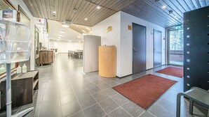 A modern hotel lobby with a wooden ceiling, grey tiled floors, a reception desk, and a large wooden pillar.