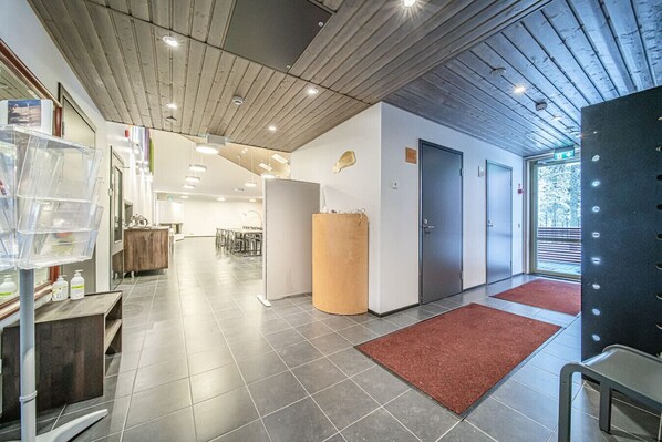 Een moderne hotellobby met een houten plafond, grijze betegelde vloeren, een receptiebalie en een grote houten zuil.
