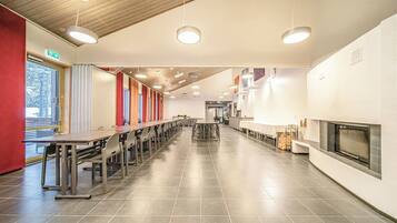 Eine großzügige Cafeteria mit langen Tischen und Stühlen, einem Kamin und Blick ins Freie.