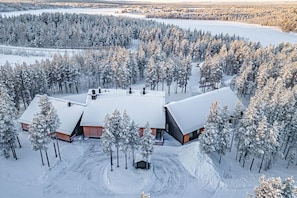Una cabaña nevada con varias cabañas, rodeada por un bosque denso.