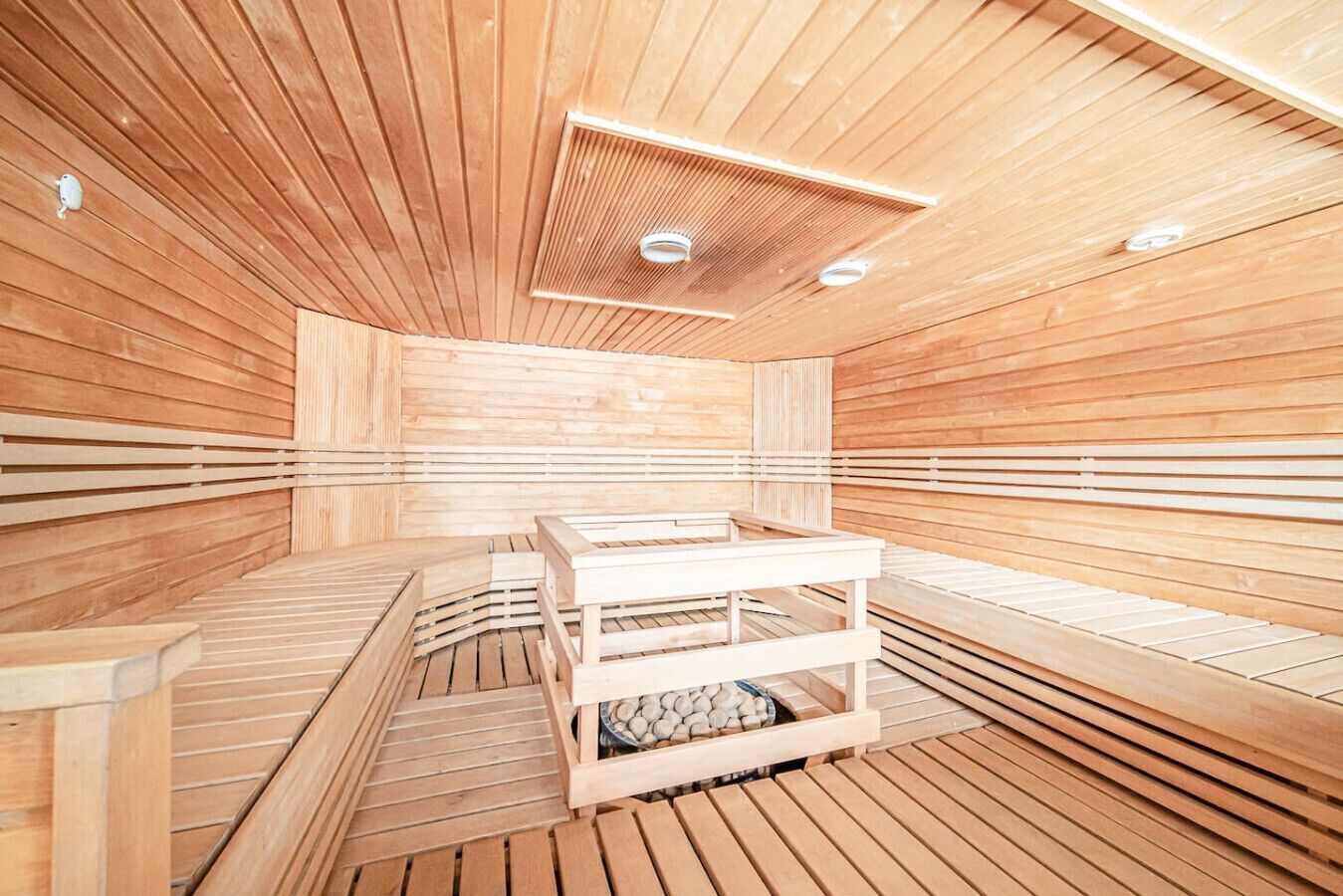 A sauna with wooden benches and a central table, featuring a sloped ceiling and built-in lighting.