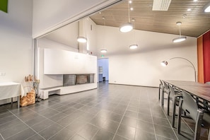 A spacious room with a fireplace, a long table with chairs, and pendant lighting. - Wellevi 1 by Aavalevi (Levi)