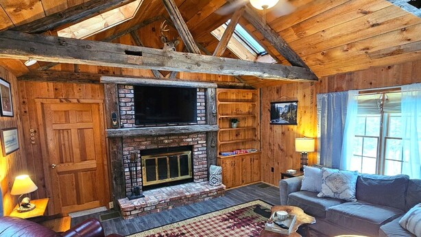 A log cabin interior with a fireplace, leather seating, and a ceiling fan. - Brant Lake Retreat–Sleeps 25 | Hot Tub | Gore Mtn. (Brant Lake)