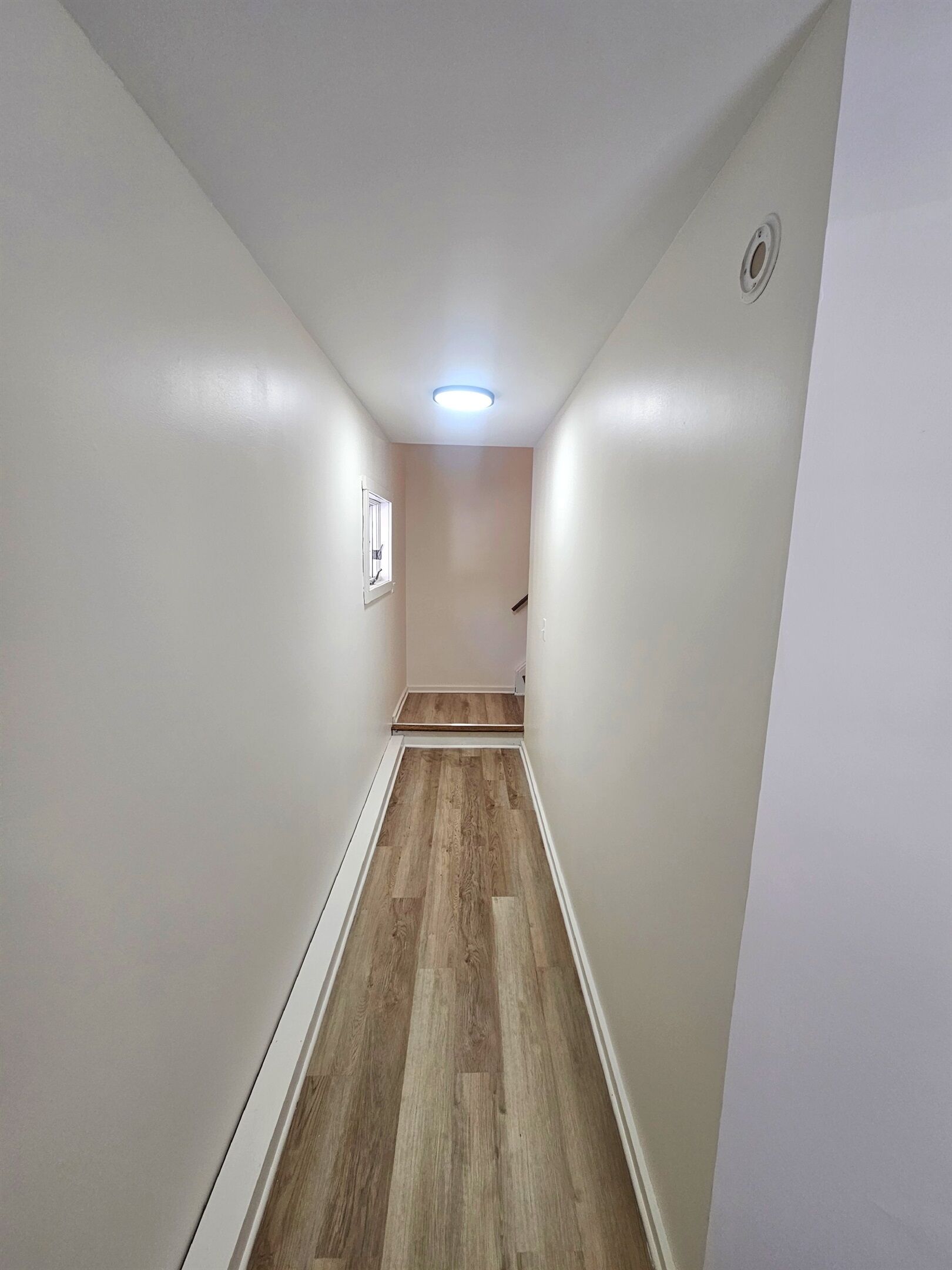 A narrow hallway with wooden flooring, white walls, and a ceiling light.