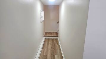 A narrow hallway with wooden flooring, white walls, and a ceiling light.