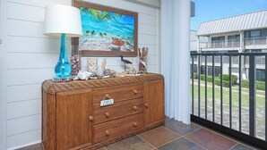 A wooden cabinet with drawers, a framed painting of a beach scene, and a blue lamp. - Bayfront Sanibel Condo Water Views Pool Mariner Pointe 712 Dolphins Reach (Sanibel Island)