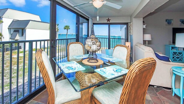 A balcony with a glass table, wicker chairs, and a ceiling fan. - Bayfront Sanibel Condo Water Views Pool Mariner Pointe 712 Dolphins Reach (Sanibel Island)