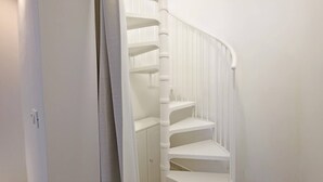Un escalier intérieur blanc, doté d’une main courante et d’une porte entrouverte.