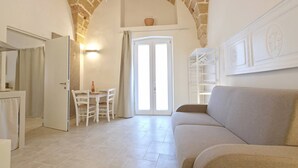 Une pièce avec une arche en pierre, une porte blanche, une table à manger avec des chaises, un canapé et un meuble blanc.