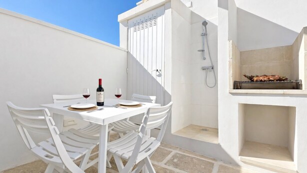 Un espace extérieur aménagé pour les repas, avec une table dressée pour deux personnes, une bouteille de vin et un barbecue.