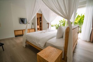 A bedroom with a four-poster canopy bed, a wooden bedside table, a TV mounted on the wall, and a view of greenery outside. - Nyuh Lengkong Beachfront Villa (Tabanan)