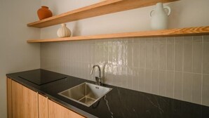 Une cuisine dotée d’un plan de travail noir, d’un évier en acier inoxydable, d’étagères en bois et d’un dosseret de crédence carrelé de couleur blanche.