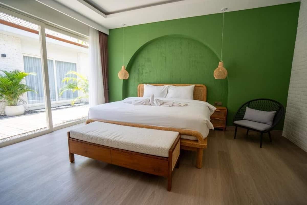 Un dormitorio con cama, banca, silla y ventanas amplias.