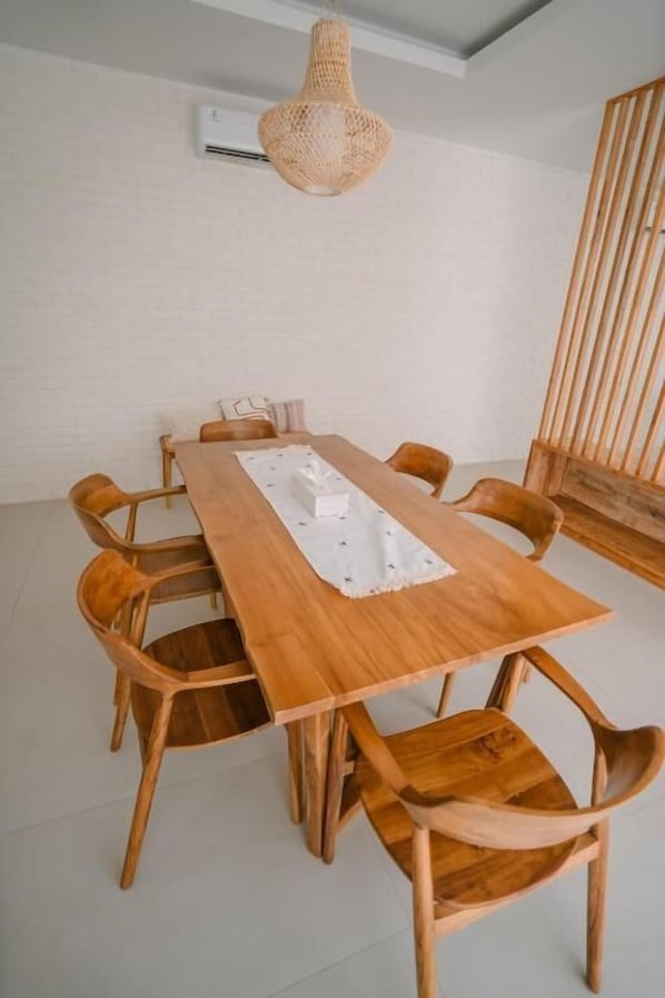 A wooden dining table with six chairs, a woven pendant light, and a white air conditioning unit on the wall.